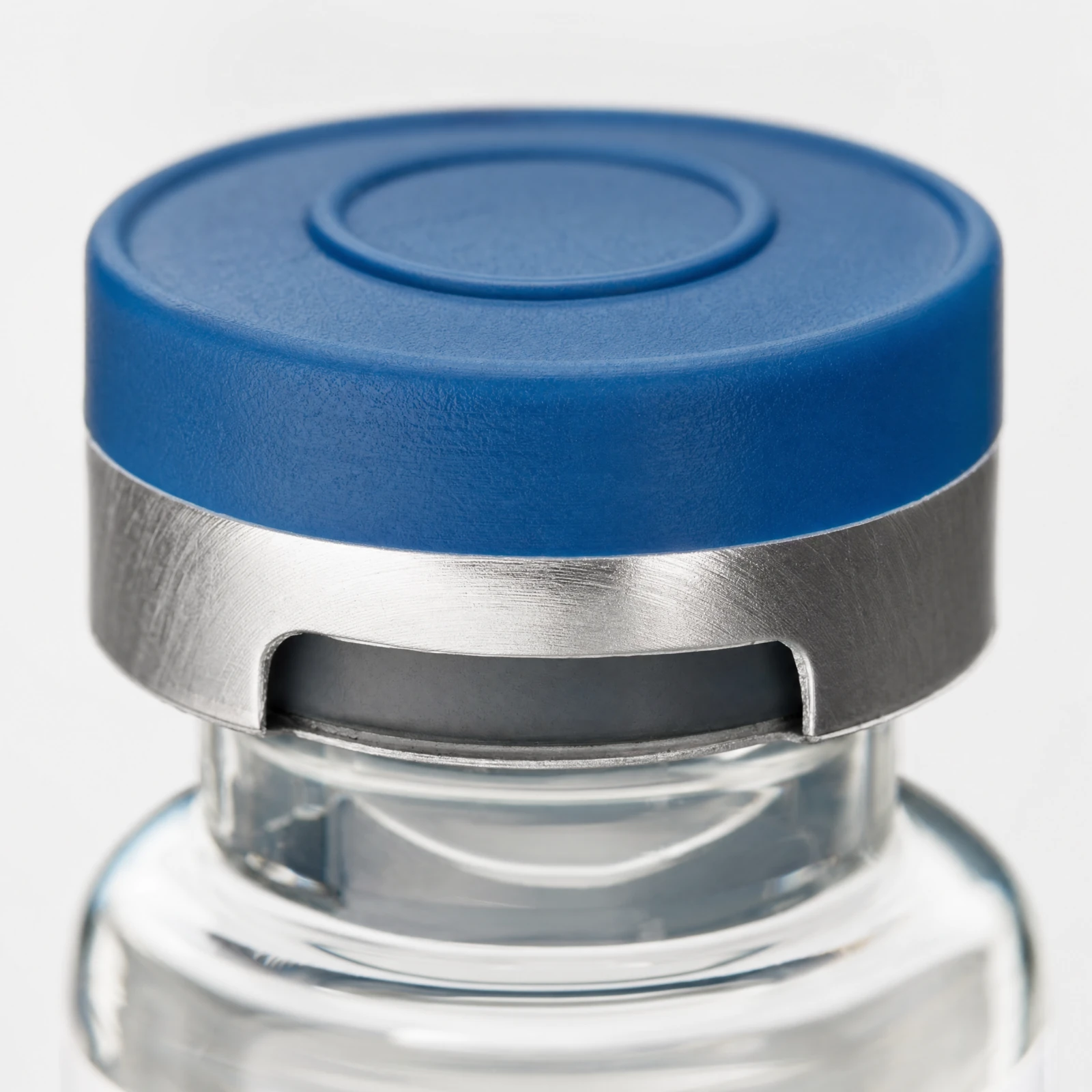 Acercamiento de la tapa azul de un vial de vidrio, con sello de aluminio y tapón de goma, sobre fondo neutro